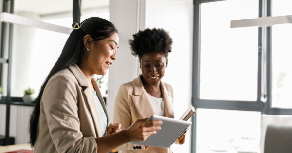Two businesswomen looking at data on digital tablet while going on a meeting