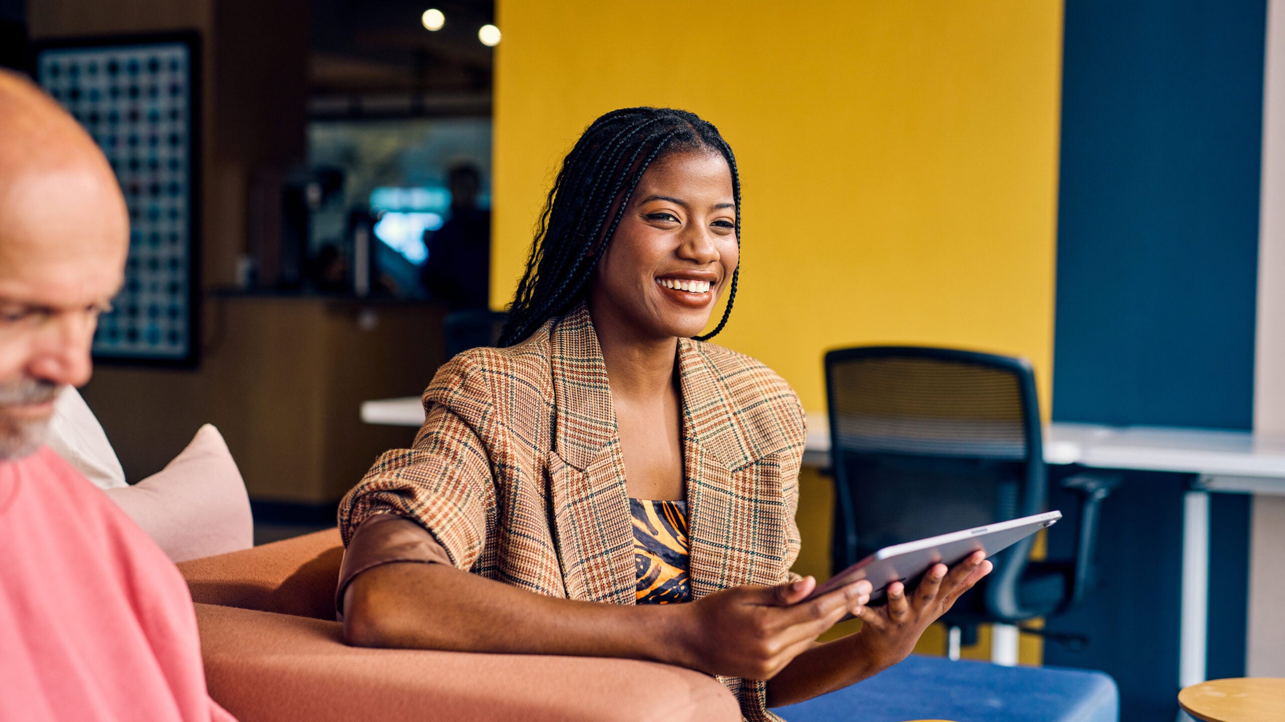 Smiling African American businesswoman in a plaid blazer holding a tablet in a modern office. Empowerment and professional growth in business concept