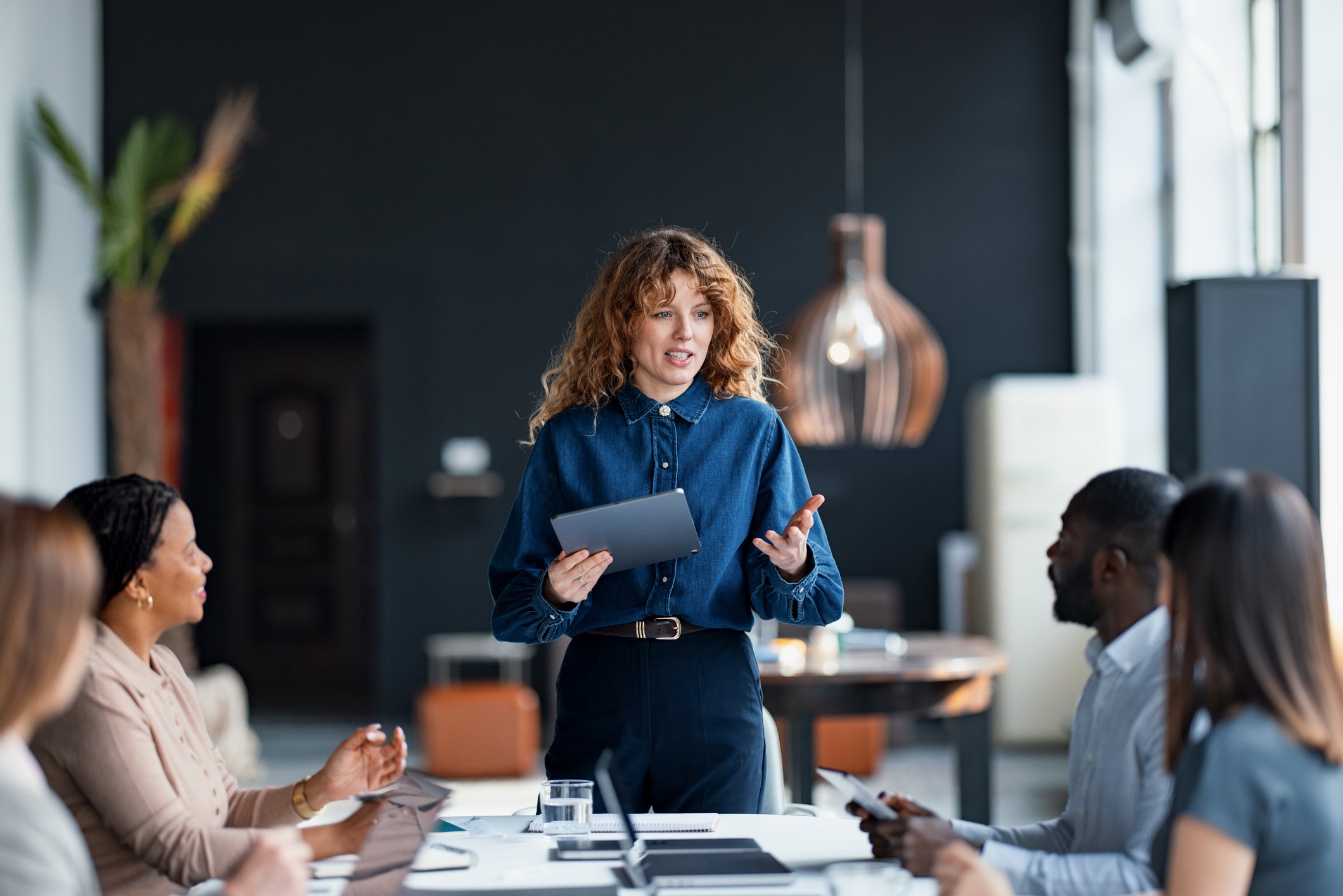 Confident businesswoman presents to a diverse team during a collaborative meeting in a stylish office environment, promoting teamwork and communication.
