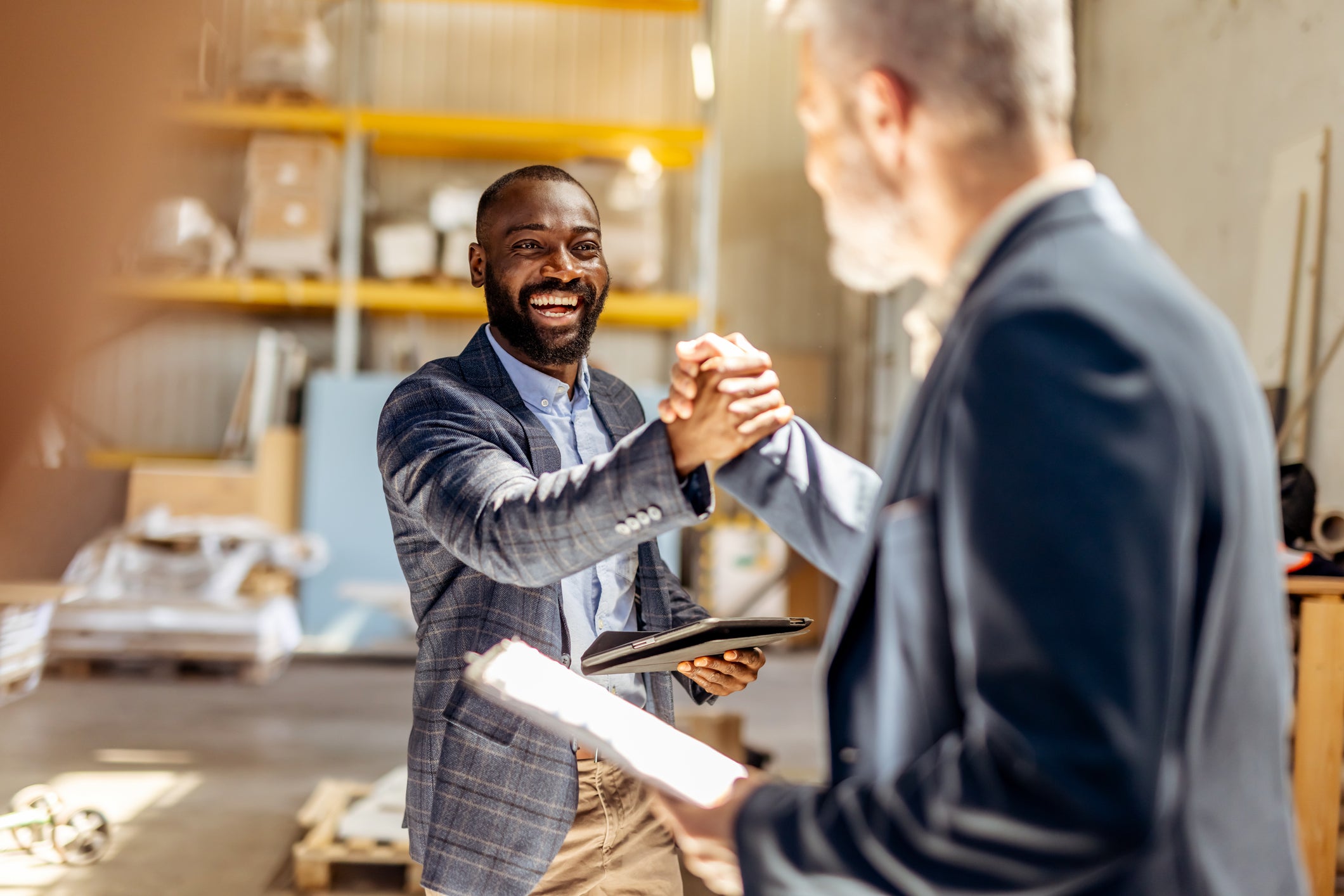 Two businessmen exchange a handshake in a modern industrial setting, exuding professionalism and collaboration. The energetic atmosphere highlights teamwork, constructive interaction, and building successful partnerships in a professional context.